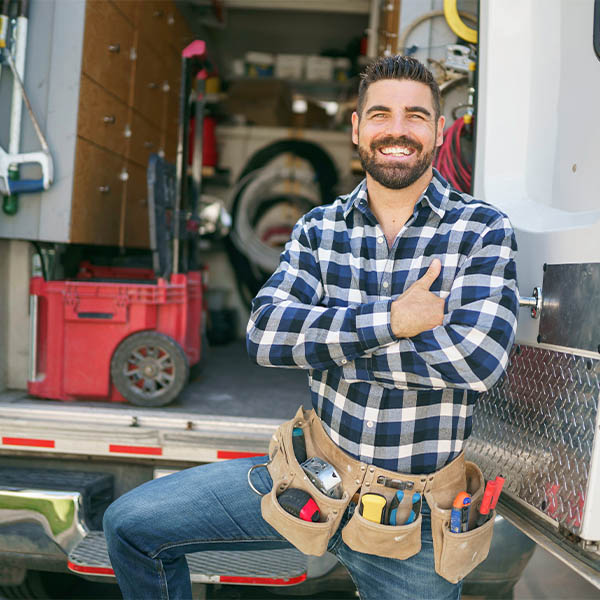 Photo of a handy man smiling standing in front of an open van filled with tools